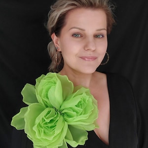 Puede incluir: Una mujer con un vestido negro y un gran broche de flor de tela verde.