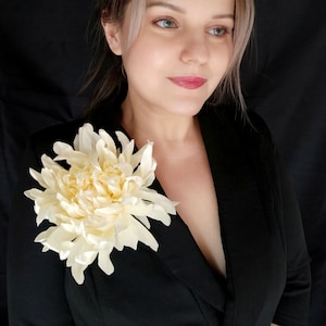 Op de afbeelding: Een vrouw draagt een zwart blazer met een grote, crèmekleurige zijden bloem die op de revers is gepind.