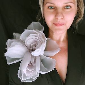 Puede incluir: Una mujer con un blazer negro con un gran broche de flor de seda blanca prendido en la solapa.