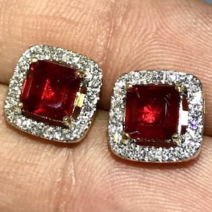 May include: A pair of gold earrings with a square red gemstone surrounded by a halo of smaller white gemstones.