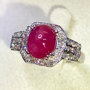 Può includere: Un anello d'argento con un grande rubino tagliato a cabochon circondato da un'aureola di diamanti più piccoli.