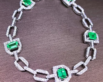 May include: A silver chain bracelet with emerald green gemstones set in square frames. The bracelet is adorned with smaller diamonds.