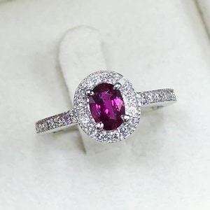 May include: A silver ring with a large oval-shaped ruby surrounded by a halo of smaller diamonds.