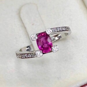 May include: A pink gemstone ring with a white gold band and small diamonds set in the band. The ring is in a red velvet ring box.