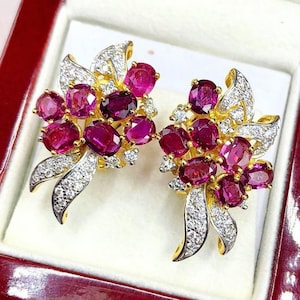 May include: A pair of gold earrings with a cluster of pink ruby stones and diamonds. The earrings are in a box with the words "Perfect Jewelry Tune" on the bottom.