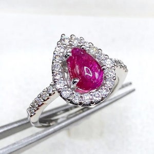 Può includere: Un anello con un rubino a forma di pera incastonato in una fascia d'argento con un alone di diamanti più piccoli.