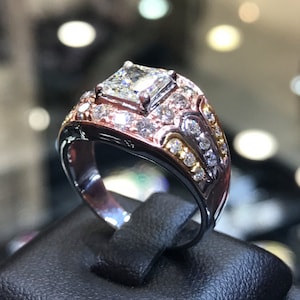 May include: A silver and rose gold ring with a large square-cut diamond in the center. The ring is set with smaller diamonds around the center stone and on the band.