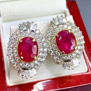 May include: A pair of ruby and diamond earrings. The earrings are oval shaped and feature a large ruby surrounded by smaller diamonds. The earrings are set in gold.