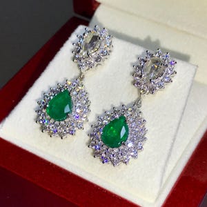 May include: A pair of emerald and diamond dangle earrings. The earrings feature pear-shaped emeralds surrounded by a halo of round diamonds. The earrings are set in white gold.