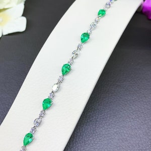 May include: A delicate silver bracelet featuring a row of pear-shaped emerald green gemstones and smaller round clear gemstones.