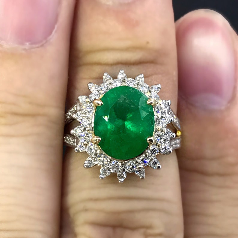 May include: A gold ring with a large oval emerald gemstone surrounded by a halo of smaller diamonds.