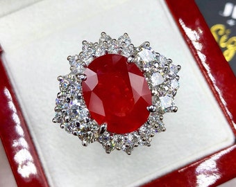May include: A red ruby ring with a halo of smaller diamonds set in white gold.