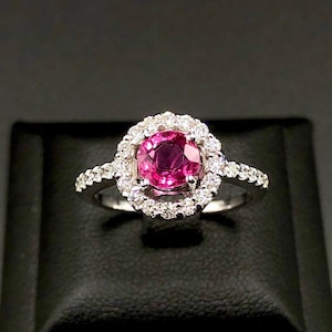 May include: A silver ring with a pink gemstone surrounded by a halo of smaller diamonds.