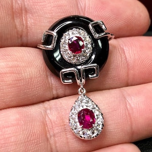 May include: A black onyx pendant with a red ruby and diamond accents. The pendant is shaped like a circle with a teardrop-shaped drop hanging from the bottom.