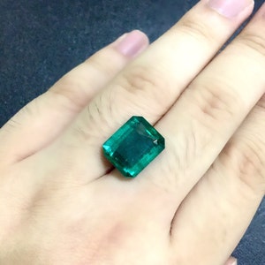 May include: A vibrant green emerald gemstone, cut in a rectangular shape, is displayed on a hand.