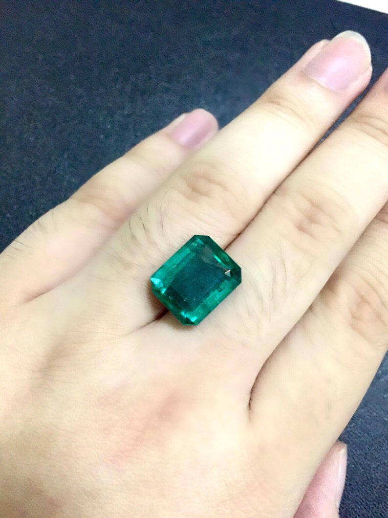 May include: A vibrant green emerald gemstone, cut in a rectangular shape, is displayed on a hand.