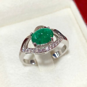 Könnte beinhalten: Ein silberner Ring mit einem großen ovalen Smaragd, der von einem Heiligenschein aus kleineren Diamanten umgeben ist.