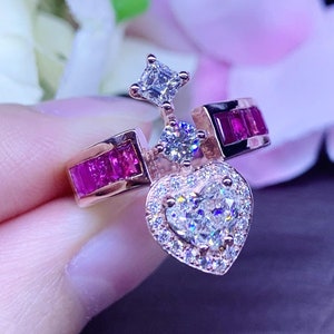 May include: Rose gold ring featuring a heart-shaped diamond center stone surrounded by smaller diamonds. The ring has a halo design and is accented with rectangular ruby stones. A square diamond and a round diamond are also featured.