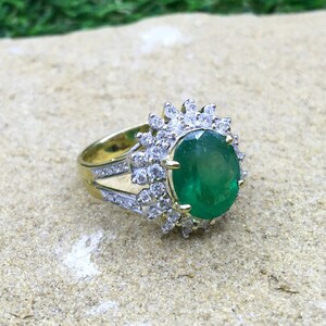 May include: A gold ring with a large oval emerald gemstone surrounded by a halo of smaller diamonds.