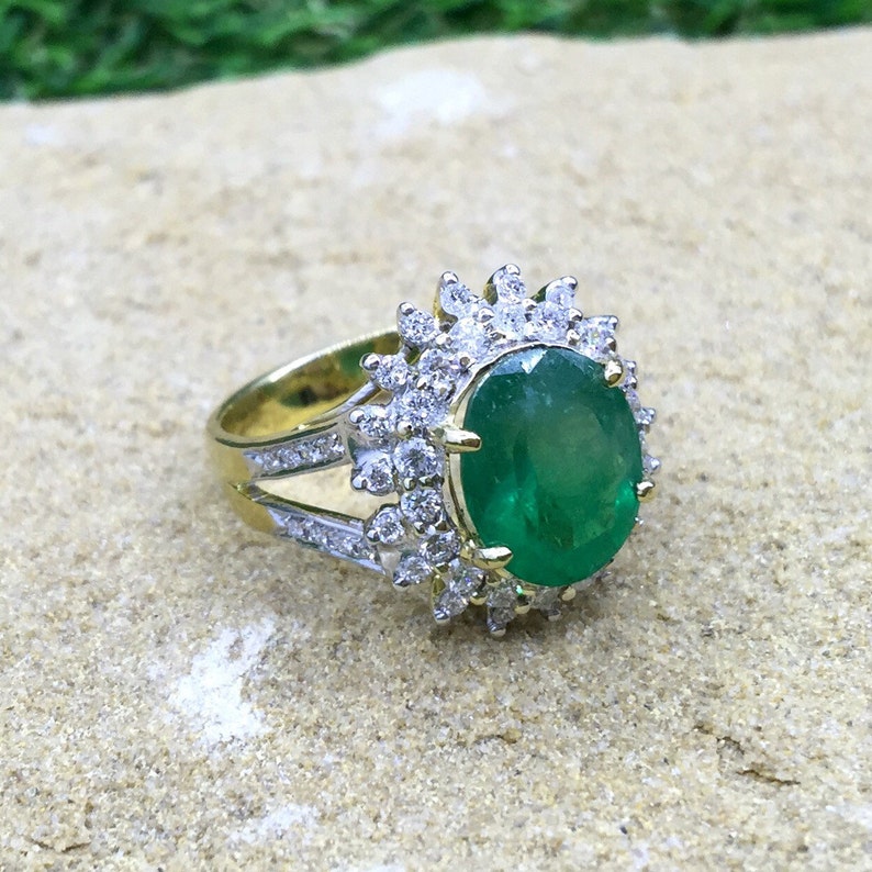 May include: A gold ring with a large oval emerald gemstone surrounded by a halo of smaller diamonds.