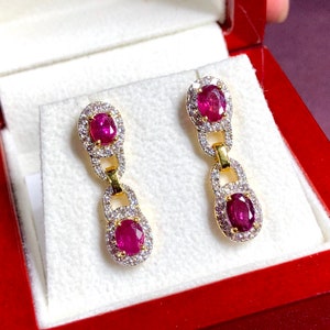May include: A pair of gold earrings with ruby and diamond accents. Each earring features a dangling chain with a ruby gemstone at the bottom.