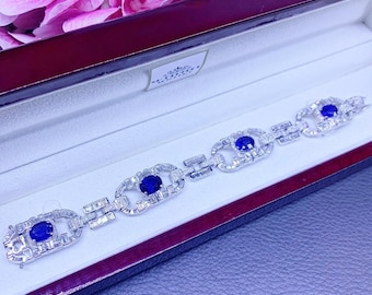 Puede incluir: Un brazalete de plata con un patrón repetido de zafiros azules ovalados y diamantes más pequeños. El brazalete se muestra en una caja de terciopelo rojo.