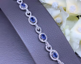 May include: A delicate silver bracelet with a chain link design. Each link features a round, blue sapphire gemstone surrounded by smaller diamonds.