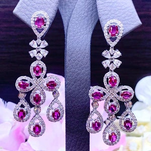 May include: A pair of dangle earrings with a silver setting and pink gemstones. The earrings feature a teardrop design with multiple pink stones.