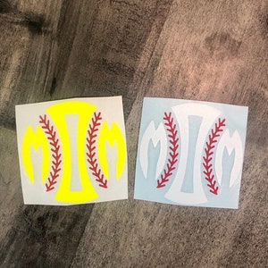May include: Two softball-themed decals. One is yellow with a red baseball stitch design, and the other is white with a red baseball stitch design. The decals are square and sit on a wooden surface.