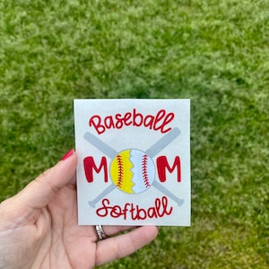 May include: A square sticker with the words "Baseball Mom Softball" in red script. The word "MOM" is in red block letters. A baseball and softball are in the center, with two crossed gray bats behind them.
