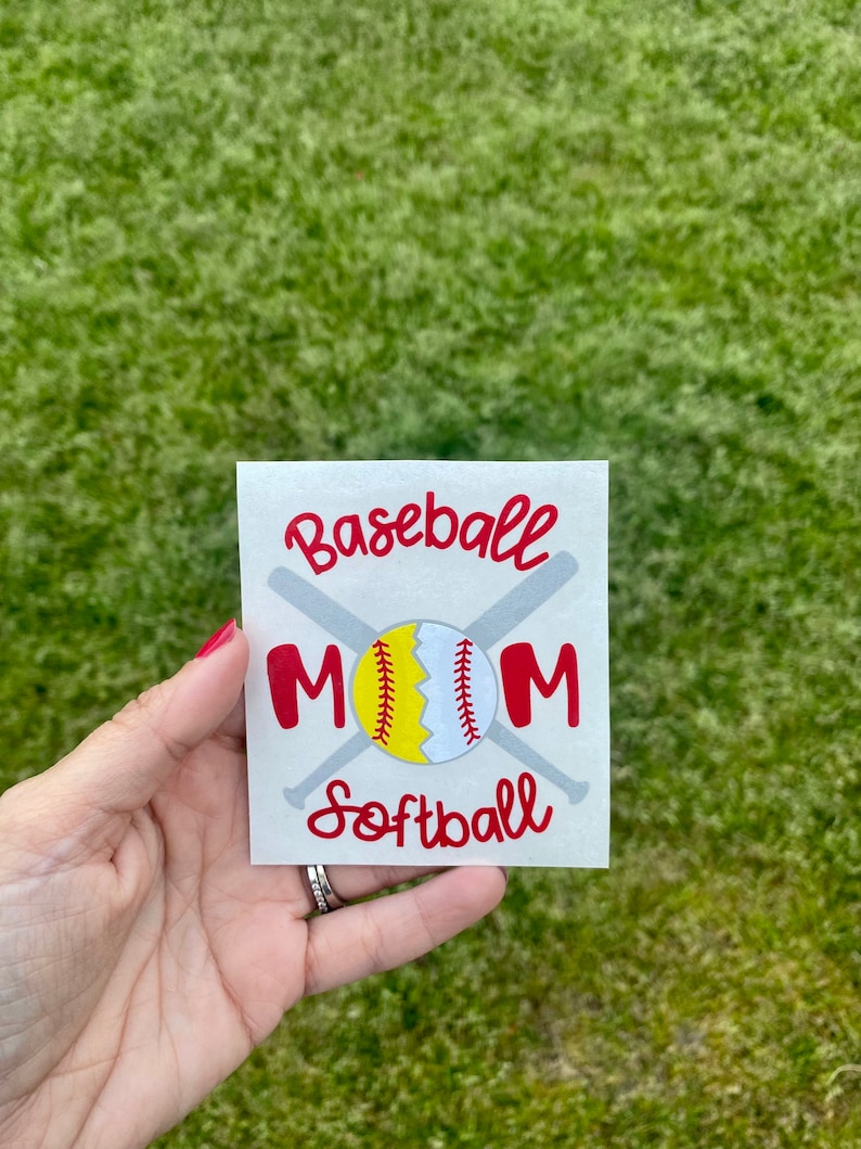 May include: A square sticker with the words "Baseball Mom Softball" in red script. The word "MOM" is in red block letters. A baseball and softball are in the center, with two crossed gray bats behind them.