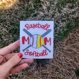 May include: A white square sticker with the words "Baseball Mom Softball" in red script. The word "MOM" is in large red letters. A baseball and two crossed bats are in the center of the sticker.