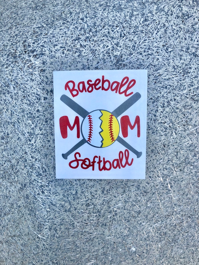 May include: A white square sign with the words "Baseball Mom Softball" in red script. A baseball and two crossed bats are in the center. The baseball is white, yellow, and red. The background is a textured silver.