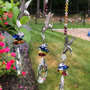 May include: Three silver hummingbird suncatchers with crystal prisms and rainbow colored beads. Each suncatcher features a hummingbird with outstretched wings and a crystal prism hanging below. The beads are arranged in a rainbow pattern, with red, orange, yellow, green, blue, indigo, and violet beads.
