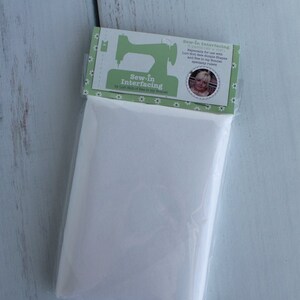 Puede incluir: Un paquete blanco de entretela termoadhesiva con una etiqueta verde que dice "Sew-in Interfacing by Lert Molt of Dee in my Bonnet". La etiqueta tambi&eacute;n tiene una m&aacute;quina de coser y una foto de una mujer.