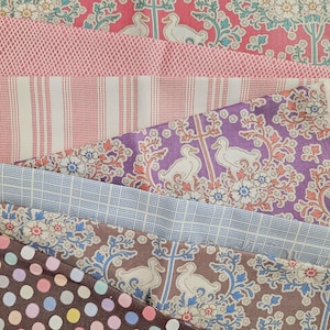 May include: A collection of fabric swatches in various patterns and colors. The fabrics include floral prints, stripes, polka dots, and a duck motif. Colors range from pink and purple to brown and blue. The fabrics are likely cotton or a similar material.