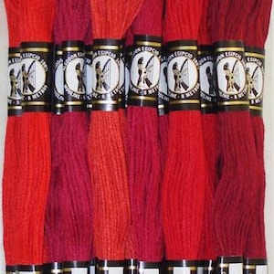 May include: Six skeins of embroidery floss in shades of red, labeled with the numbers 1166, 1667, 1490, 1906, 1902, 1915. The floss is packaged with a label that reads "Presencia America A Colonial Needle Company Finca Mouliné Floss Sampler SCARLET".