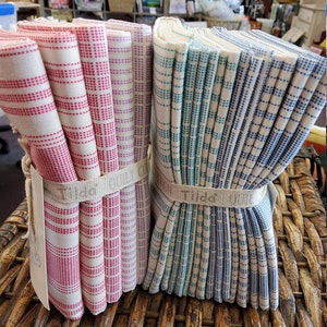 May include: Two stacks of kitchen towels, one pink and white, the other blue and white, with a white background and a woven pattern.