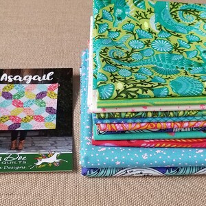 May include: A stack of 10 colorful fabric squares with a seahorse and coral design. The fabric squares are stacked on a brown surface. A card with the text "Asagaail" and "Running Doe Quilts" is in the foreground.