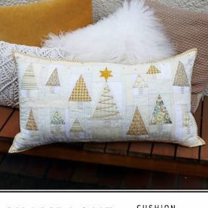 Puede incluir: Un cojín blanco y dorado con un diseño acolchado de árboles de Navidad estilizados. El cojín está etiquetado como "Champagne Christmas Cushion Pattern by Louise Papas".