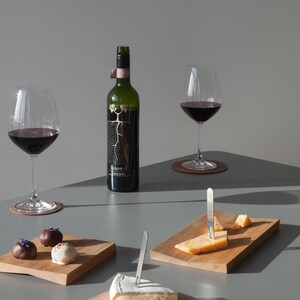 May include: A dark green wine bottle labeled Root: 1, two stemmed glasses filled with red wine, three rectangular wooden serving boards, two silver metal cheese forks, assorted cheese wedges, and three chocolate truffles with floral garnishes.