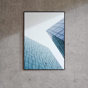 May include: Framed architectural photograph featuring two modern skyscrapers with blue-tinted glass facades against a pale sky. The buildings are set against a textured gray concrete wall.