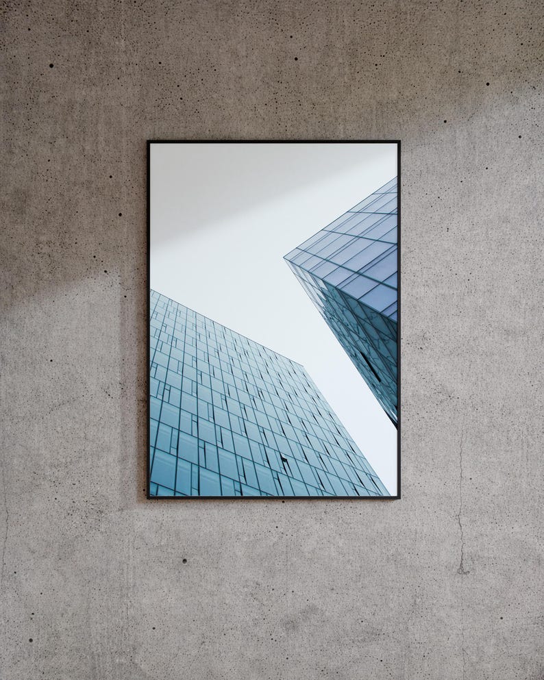 May include: Framed architectural photograph featuring two modern skyscrapers with blue-tinted glass facades against a pale sky. The buildings are set against a textured gray concrete wall.