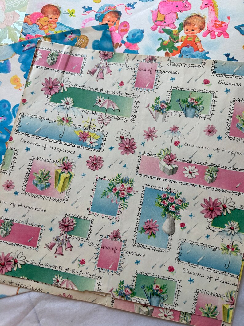 Puede incluir: Una hoja de papel de regalo vintage con fondo blanco y un patr&oacute;n repetitivo de dise&ntilde;os florales rosas, azules y verdes. El papel tiene el texto "Showers of Happiness" impreso en &eacute;l.