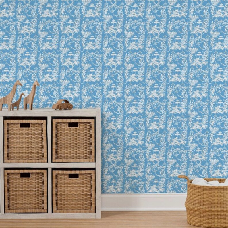 May include: A blue wallpaper with a white repeating pattern of stylized trees and flowers. The wallpaper is displayed in a room with a white shelf unit with six woven baskets and a toy car on top. A wicker basket with white fabric inside is on the floor.