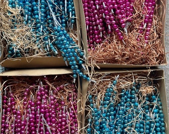 May include: Four boxes filled with bundles of iridescent blue and pink glass beads. The beads are strung on silver wire and are arranged in a decorative pattern. The boxes are filled with brown packing material.