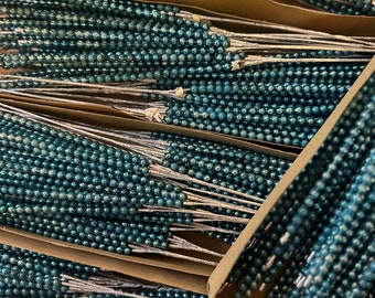 May include: A close-up of a box filled with teal blue beaded stems. The stems are arranged in rows and are ready to be used for crafting or decorating.
