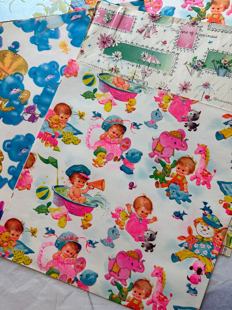 Puede incluir: Papel de regalo blanco con un patr&oacute;n repetido de animales beb&eacute;s rosas y azules, incluyendo elefantes, jirafas y patos. El papel tambi&eacute;n presenta beb&eacute;s con vestidos rosas y azules y un beb&eacute; en una ba&ntilde;era. El texto "Showers of Happiness" aparece en la esquina superior derecha.
