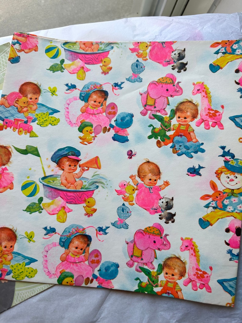 Puede incluir: Un papel de regalo para baby shower rosa y blanco con un patr&oacute;n repetitivo de beb&eacute;s, animales y juguetes. El papel presenta una variedad de colores, incluyendo rosa, azul, amarillo, verde y marr&oacute;n. Los beb&eacute;s est&aacute;n todos vestidos con ropa rosa y blanca, y los animales incluyen elefantes, jirafas y tortugas. Los juguetes incluyen una pelota, una ba&ntilde;era y un barco de juguete.