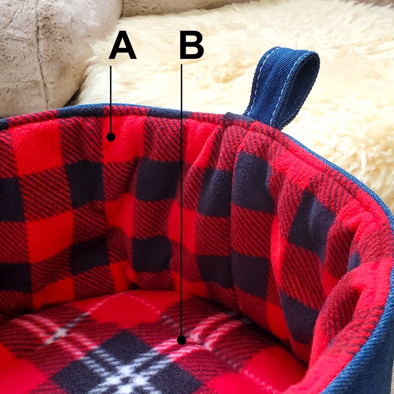 May include: A round pet bed with a red and black plaid interior and a blue denim exterior. The bed has a soft, plush texture and a sturdy handle for easy carrying. The plaid pattern is a classic design.